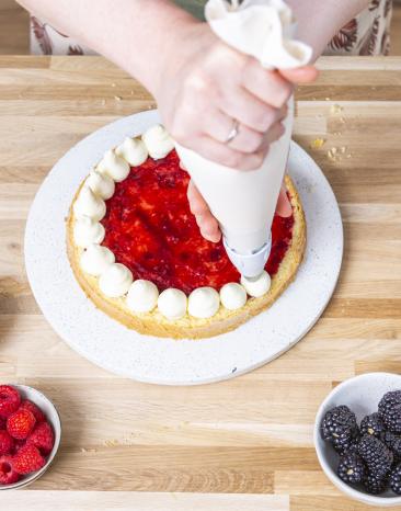 Sahnecreme wird mit Spritzbeutel auf Tortenboden getupft.