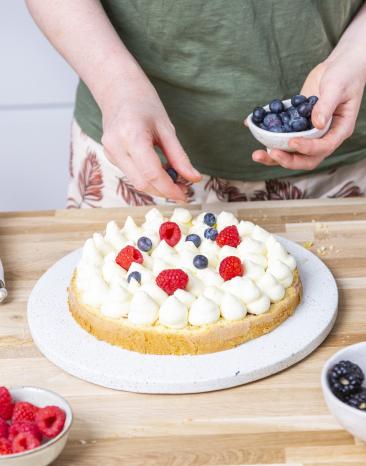 Beeren werden auf Sahnecreme auf Torte verteilt.