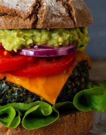 Burger mit Grünkohlpatty auf einem Stück Backpapier auf einem Holztisch