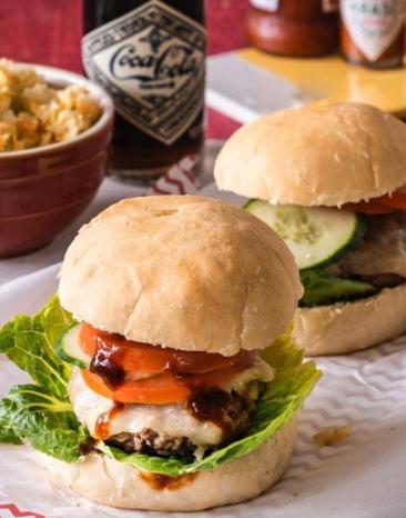 Zwei Cheeseburger mit Coleslaw auf einem Tisch, daneben Sauce