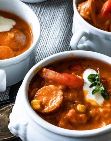 Deftiges Wurstgulasch in drei Schüsseln, die auf einem Holztablett stehen