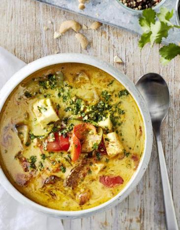 Gemüse-Curry "Jalfrezi" in einer weißen Schale auf einem Holztisch, daneben ein Löffel