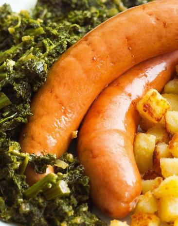 Grünkohl mit Wurst und Röstkartoffelwürfeln auf einem weißen Teller