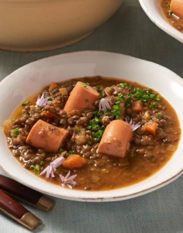 Schwäbische Linsensuppe angerichtet in einem tiefen Teller, daneben goldenes Besteck