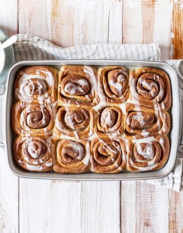 Vegane Zimtschnecken in Auflaufform mit weißem Guss in Schälchen.