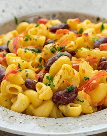 Pasta mit Bohnen, roter Paprika und Nacho-Käsesauce in einem tiefen Teller auf einem Holzbrett