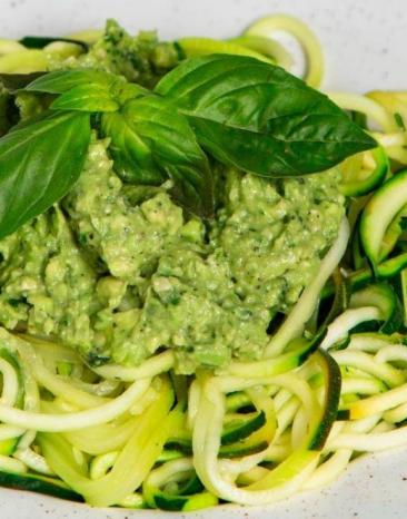 Zoodles mit Avocadopesto angerichtet n einem tiefen Teller, darauf Basilikumblätter