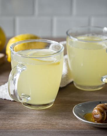 Heiße Zitrone in zwei Glastassen mit Zitronen im Hintergrund.
