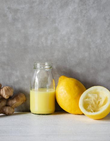 Ingwer-Zitrone-Shot in einer Glasflasche, daneben Zitronen und Ingwerknollen