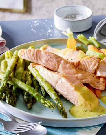 Grüner Spargel mit Lachs und Senf-Butter auf einem Teller angerichtet.