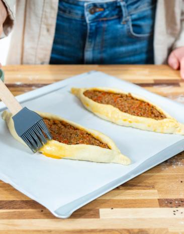 Pide mit Hackfleisch wird mit verquirltem Ei bestrichen. 