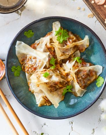 Gedämpfte Dumplings mit Gemüse auf einem blauen Teller.