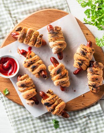 Hotdog-Stockbrot mit Röstzwiebeln auf einem Holzbrett.