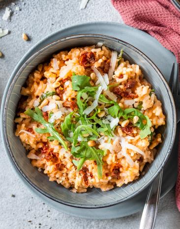 Risotto mit getrockneten Tomaten, Pinienkernen und Rucola in einer Schüssel.