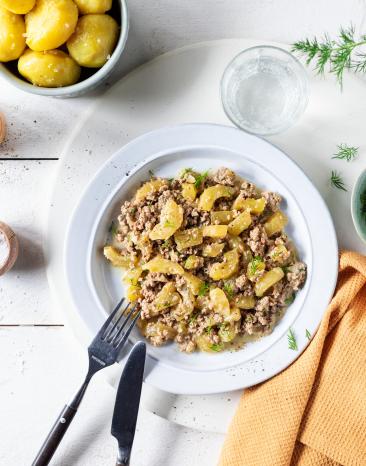 Schmorgurken mit Hackfleisch auf einem weißen Teller, dazu Kartoffeln.