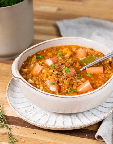 Linsensuppe mit Würstchen in einer hellen Schüssel mit Löffel.