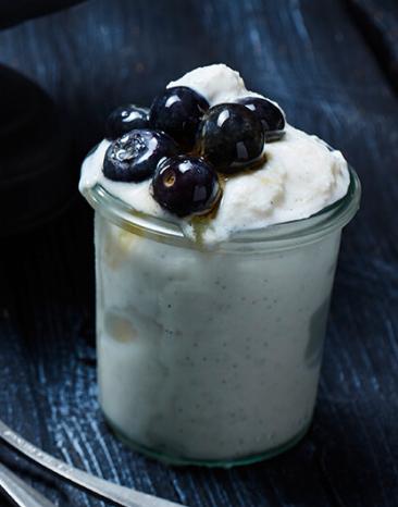 Cremiger Frozen Joghurt im Glas mit Heidelbeeren getoppt.