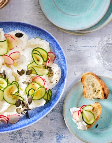 Ricotta auf einem Teller mit Zucchini, Radieschen und Kürbiskernen.