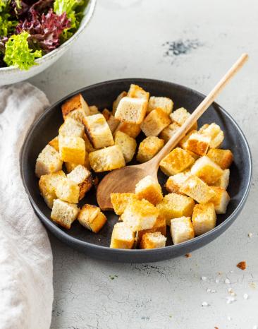 Croûtons in einer schwarzen Schale mit Holzlöffel.