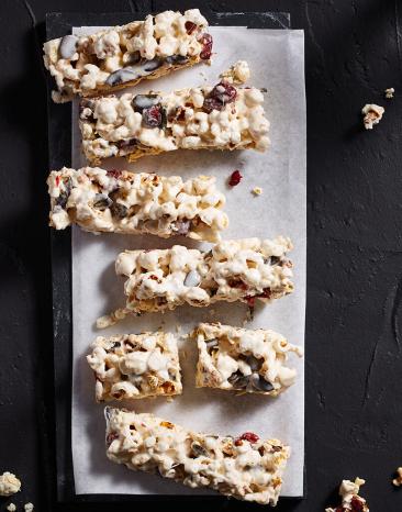 Müsliriegel mit Popcorn auf hellem Backpapier auf einem schwarzen Untergrund.