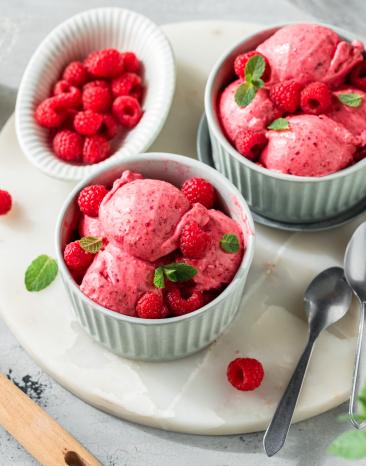 Himbeereis in Kugeln mit frischen Himbeeren und Minze dekoriert.