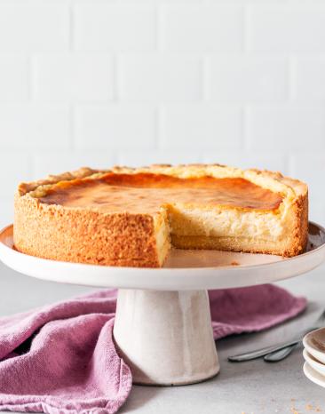 Veganer Käsekuchen auf einer Tortenplatte, angeschnitten.