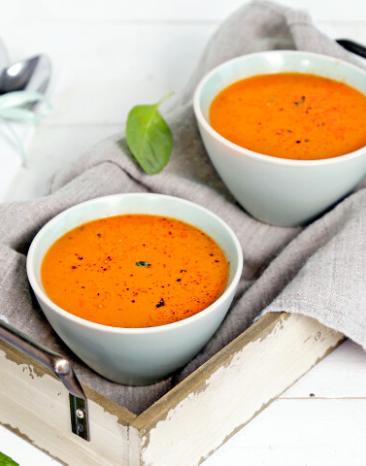 Cremige Tomatensuppe in hellen Schüsseln auf Tüchern.
