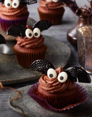 Fledermaus-Cupcakes mit Zuckeraugen und Keksflügeln dekoriert.
