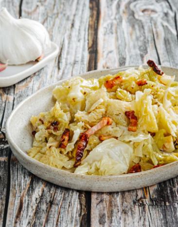 Kohl mit gebratenem Knoblauch und Speck auf einem Teller.