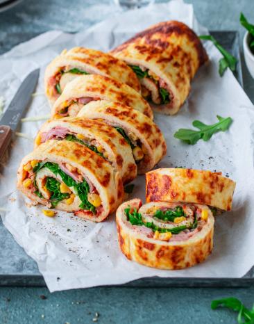 Low-Carb-Pizzarolle aufgeschnitten mit einem Messer auf einem Brett mit Papier angerichtet.