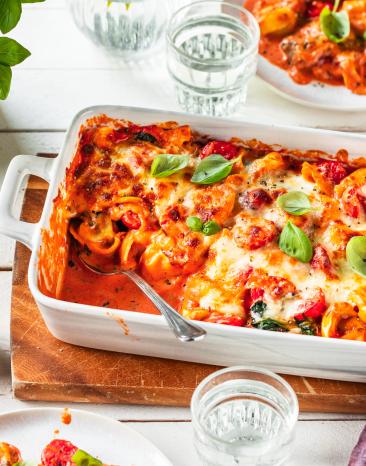 Tortellini Auflauf auf einem gedeckten Tisch in einer weißen Auflaufform.