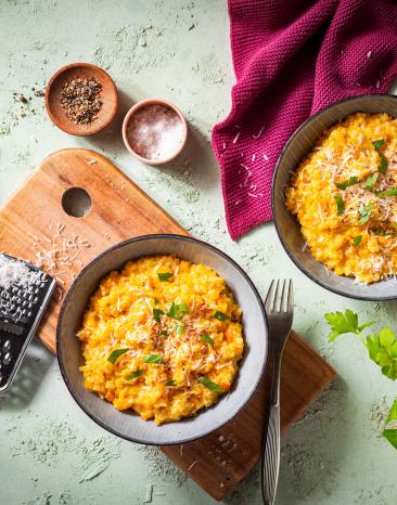 Kürbis Risotto in Schüsseln auf einem Holzbrett mit geriebenem Parmesan.