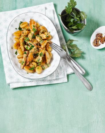 Ein Teller mit Gnocchi und Hähnchen mit Petersilie und Sauce garniert.