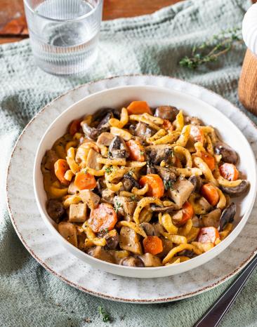 Spätzle mit Pilzragout in einem tiefen, weißen Teller auf einem Tuch.