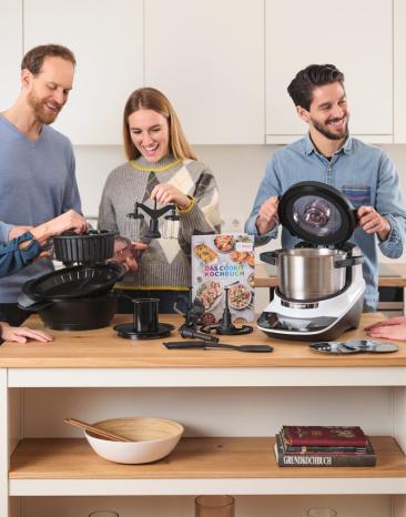 Der Cookit steht mit seinen Tools auf der Küchezeile und fünf Leute betrachten diese. 