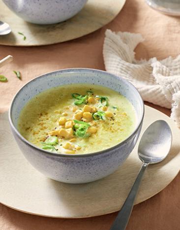 Kokos Suppe mit Mais in einer Schüssel getoppt mit Frühlingszwiebeln.