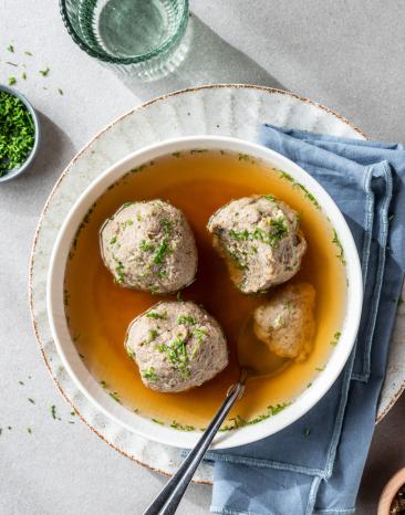 Leberknödel in einer kräftigen Brühe in einer weißen Schüssel.