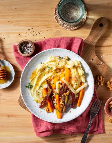 Pastinaken Püree getoppt mit Wurzelgemüse auf einem Teller auf einem gedeckten Tisch mit Honig.