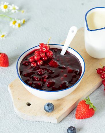 Rote Grütze in Schale angerichtet mit Beeren und Vanillesauce