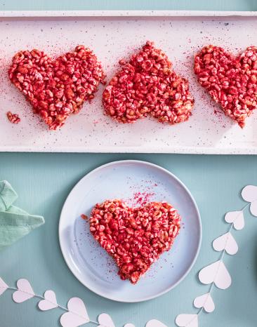 Kleine rote Herzen aus Himbeeren und Marshmallows auf einer rosa Servierplatte