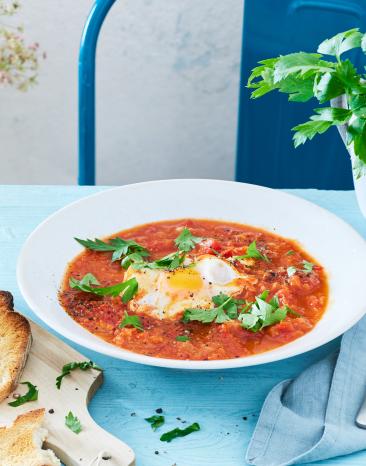 Shakshuka in einem hellen Teller mit Ei und Basilikum.