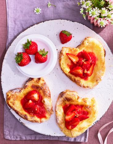 Erdbeer Blätterteig Herzen mit frischen Erdbeeren auf einem Teller.