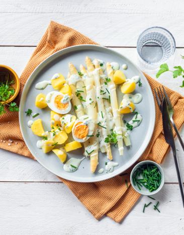 Spargel, kartoffeln, gekochtes Ei mit Kräuter Béchamel auf einem Teller angerichtet.