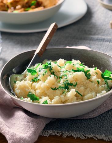 Blumenkohlreis in einer Schüssel mit Löffel und Kräutern garniert.