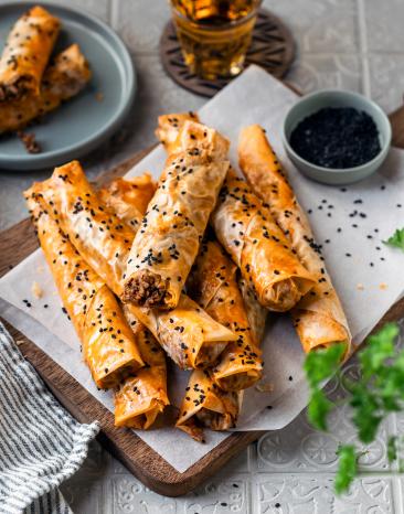 Börek mit Hackfleischfüllung knusprige Teigröllchen auf einem Brett.