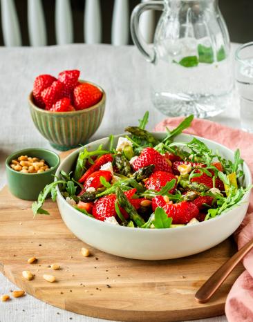Spargelsalat mit Erdbeeren in einer Schüssel auf einem gedeckten Tisch.