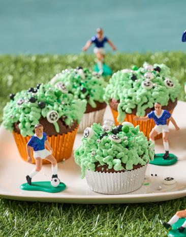 Fußball Muffins mit grünem Frosting und kleinen Fußball Figuren daneben.