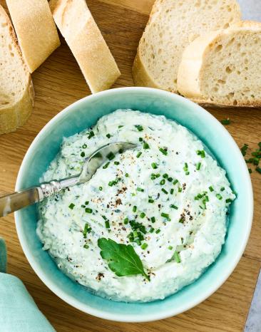 Schmand Kräuter Dip in einer kleinen Schüssel, daneben aufgeschnittenes Baguette.
