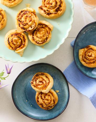 Schnelle Pizzaschnecken aus Blätterteig auf bunten Tellern.