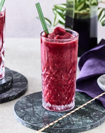 Cola Slush Eis mit Kirsche in zwei Gläsern mit Stohhalmen.